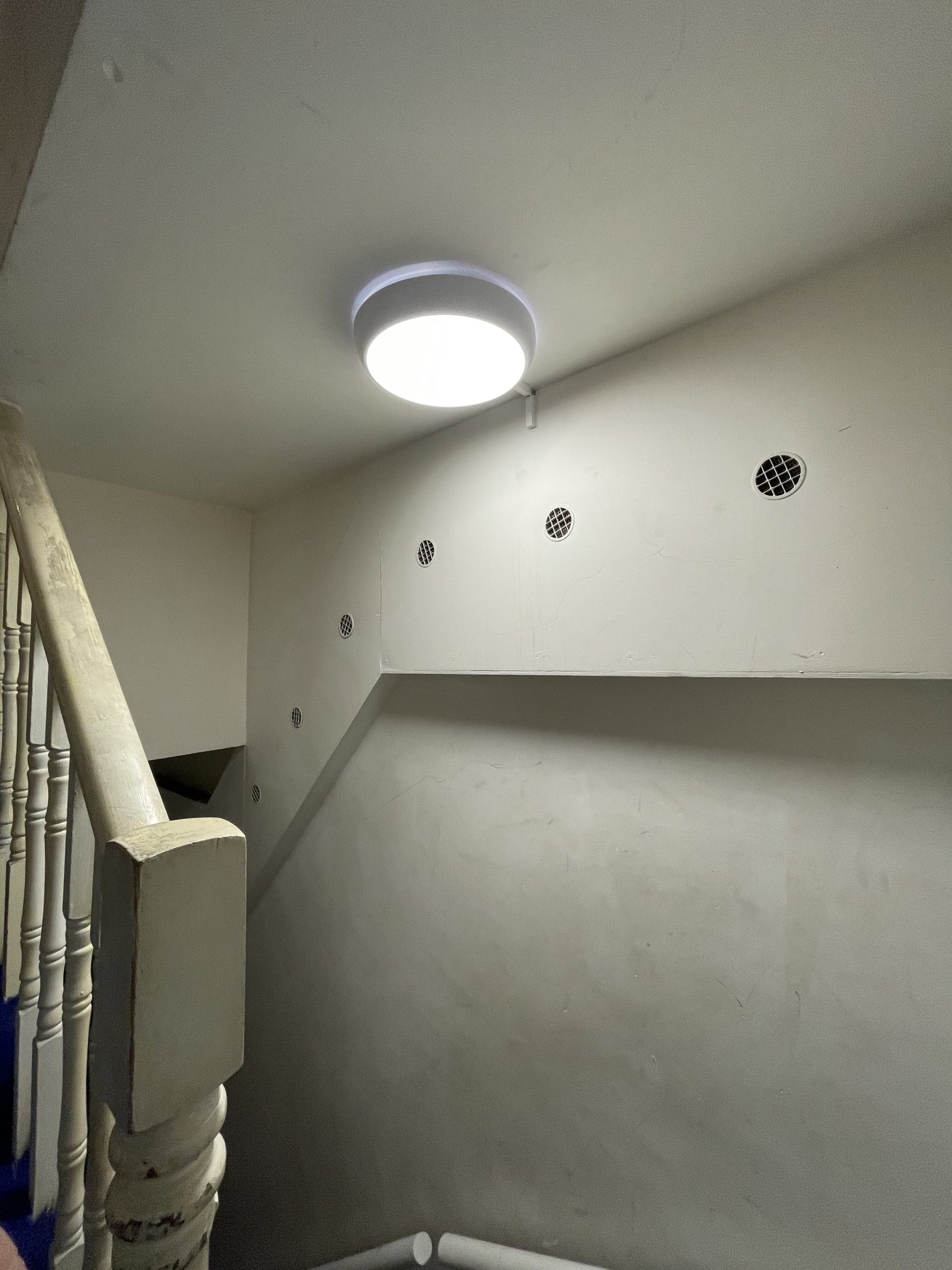 Lighting installation in property staircase, modern ceiling light, vent grilles on wall, pristine white walls, maintained property management.