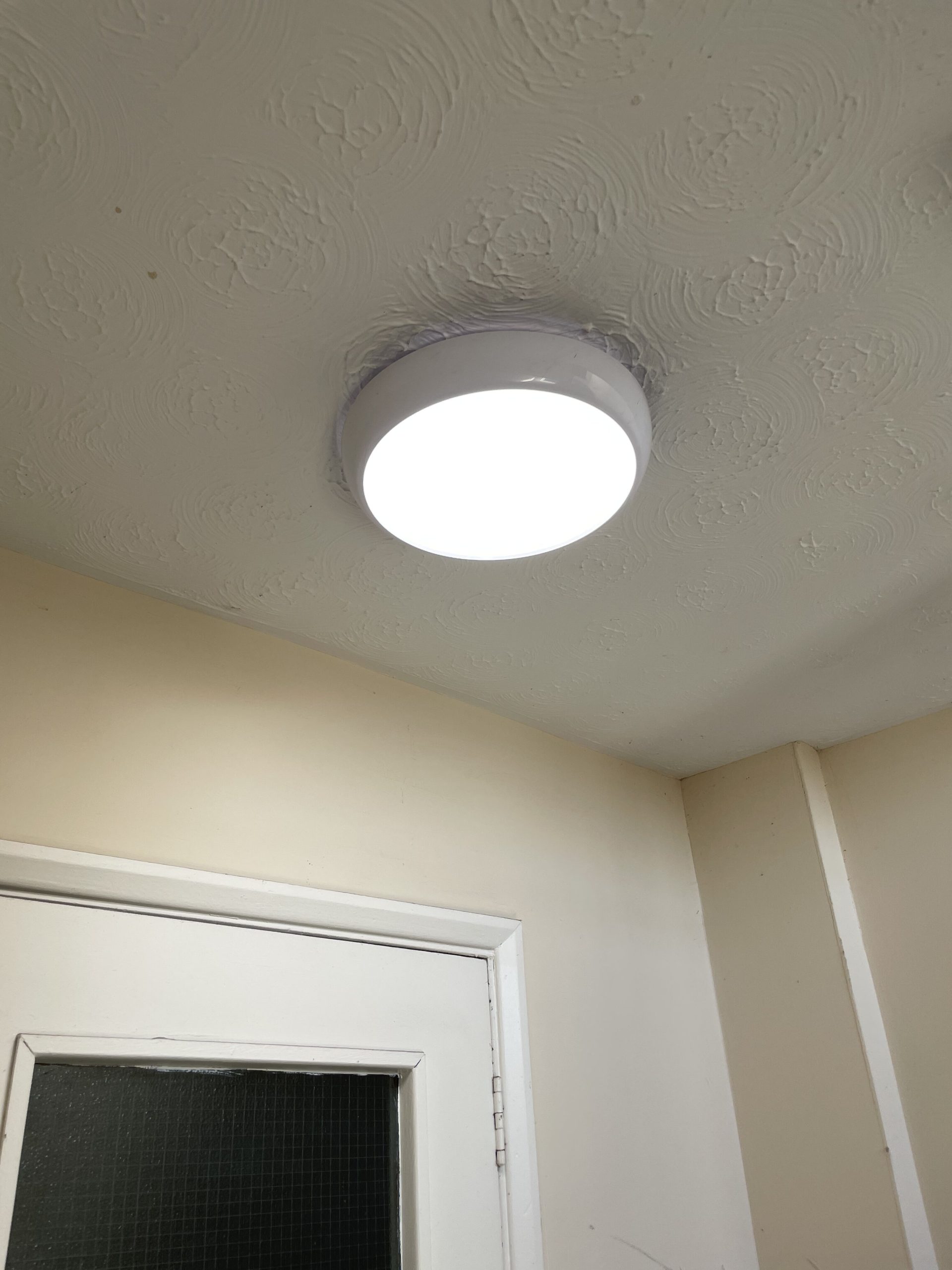 Ceiling-mounted LED light installed in a room with textured ceiling and a door frame. Perfect for property management and electrical upgrades.