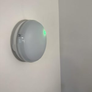 Smart smoke detector on white wall, green LED light.